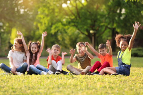 Cute little children sitting on grass outdoors on sunny day